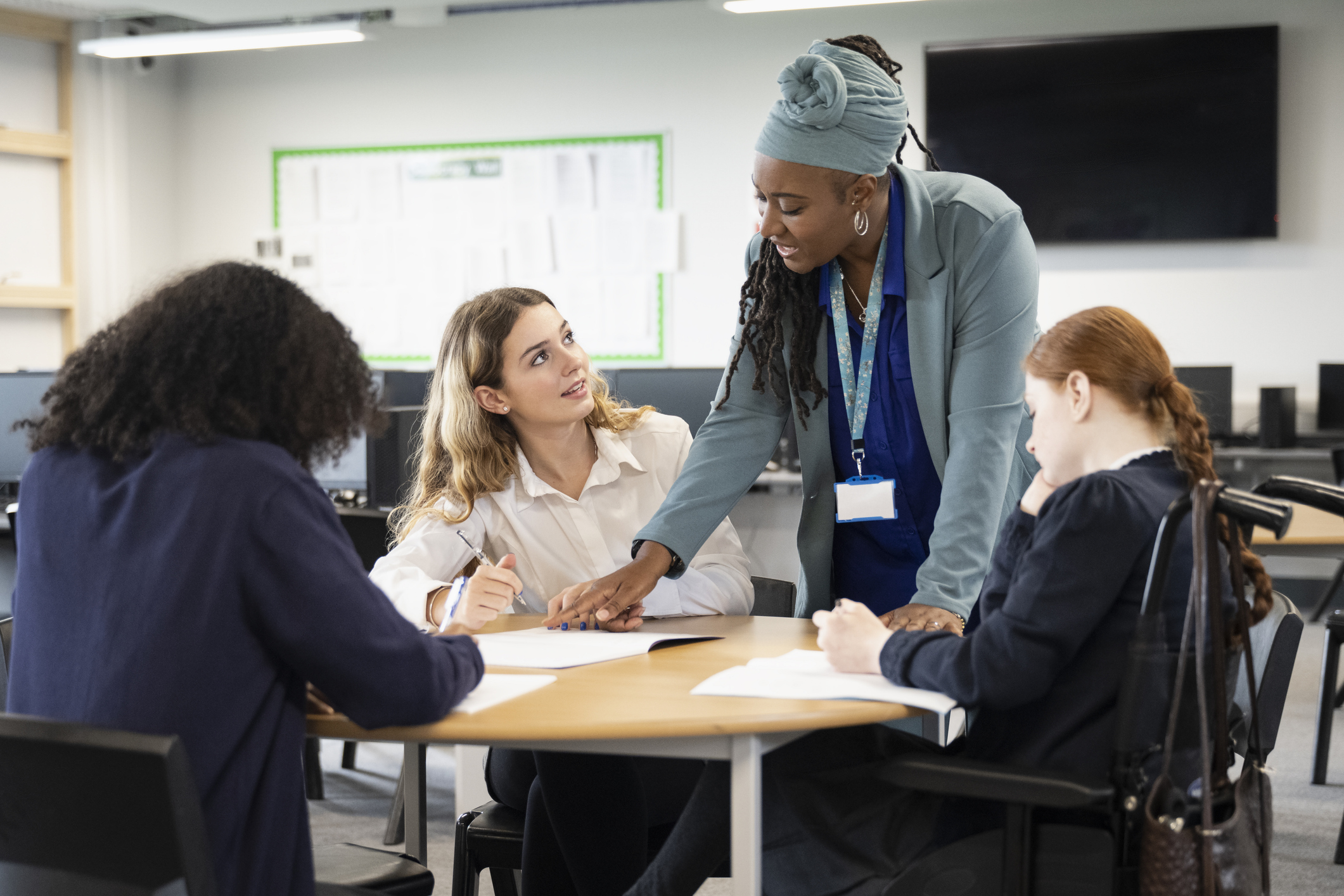 Vrouwelijke studenten zitten aan een tafel terwijl een docent uitleg geeft. Een van de studenten zit in een rolstoel.